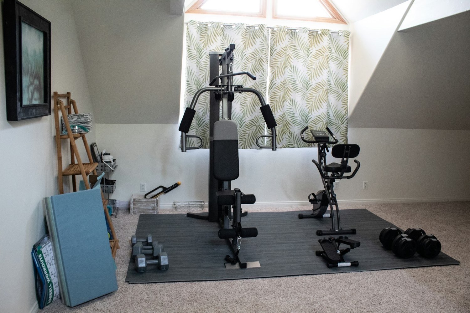 A home gym with a strength machine and bike under a sloped ceiling